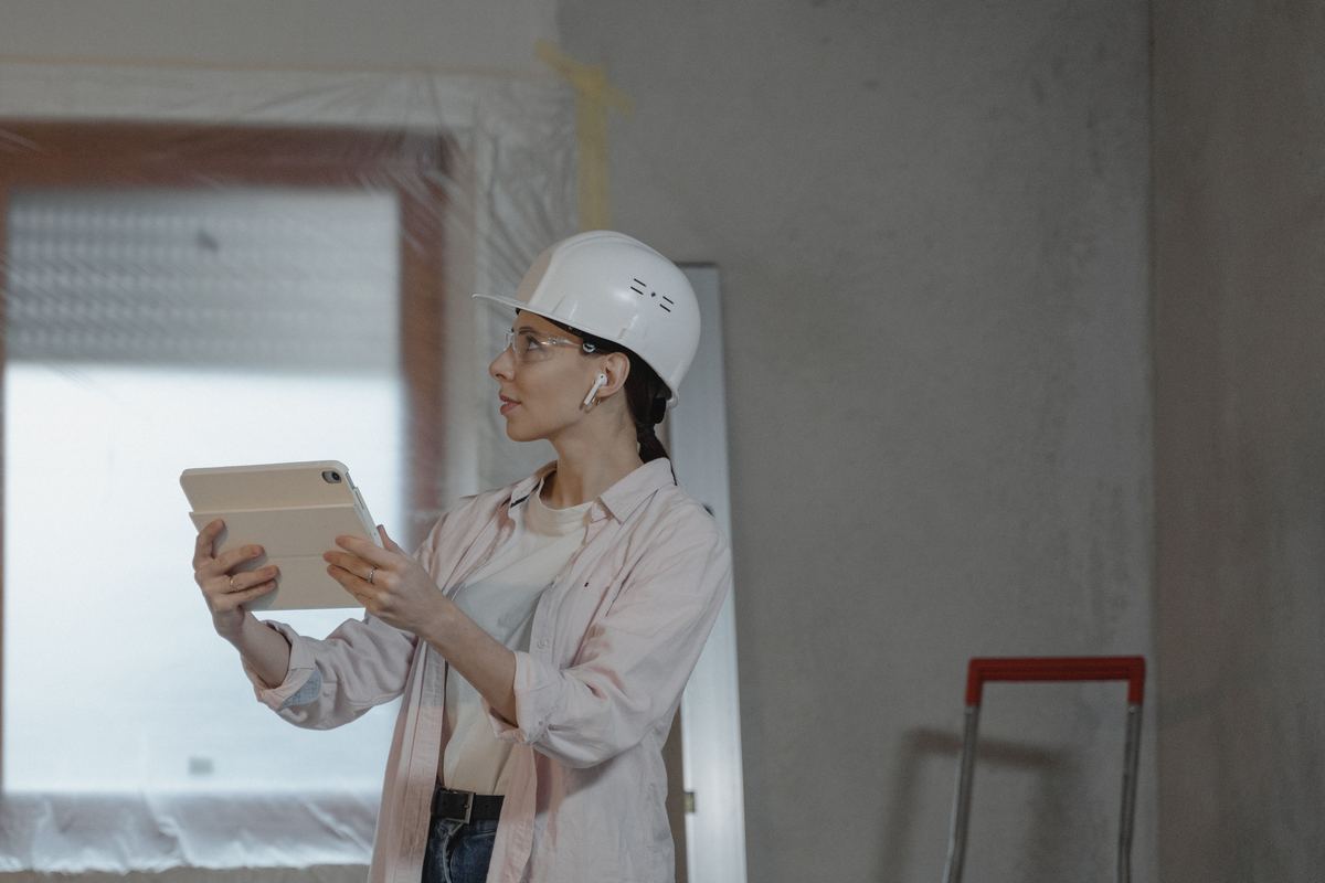 Professionnelle du bâtiment avec un casque de chantier, consultant une tablette dans une pièce en rénovation